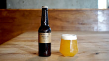 Load image into Gallery viewer, Bottle and glass of beer on a wooden surface with a blurred background