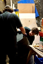 Load image into Gallery viewer, Two people moving a barrel through a dimly lit brewery.
