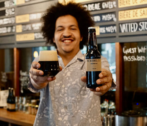 Man holding a bottle and glass of beer in a bar setting