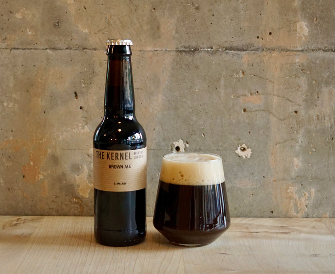 Bottle and glass of The Kernel Brown Ale against a textured wall.
