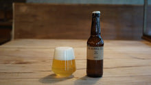 Load image into Gallery viewer, Beer bottle and glass on a wooden surface with a blurred background
